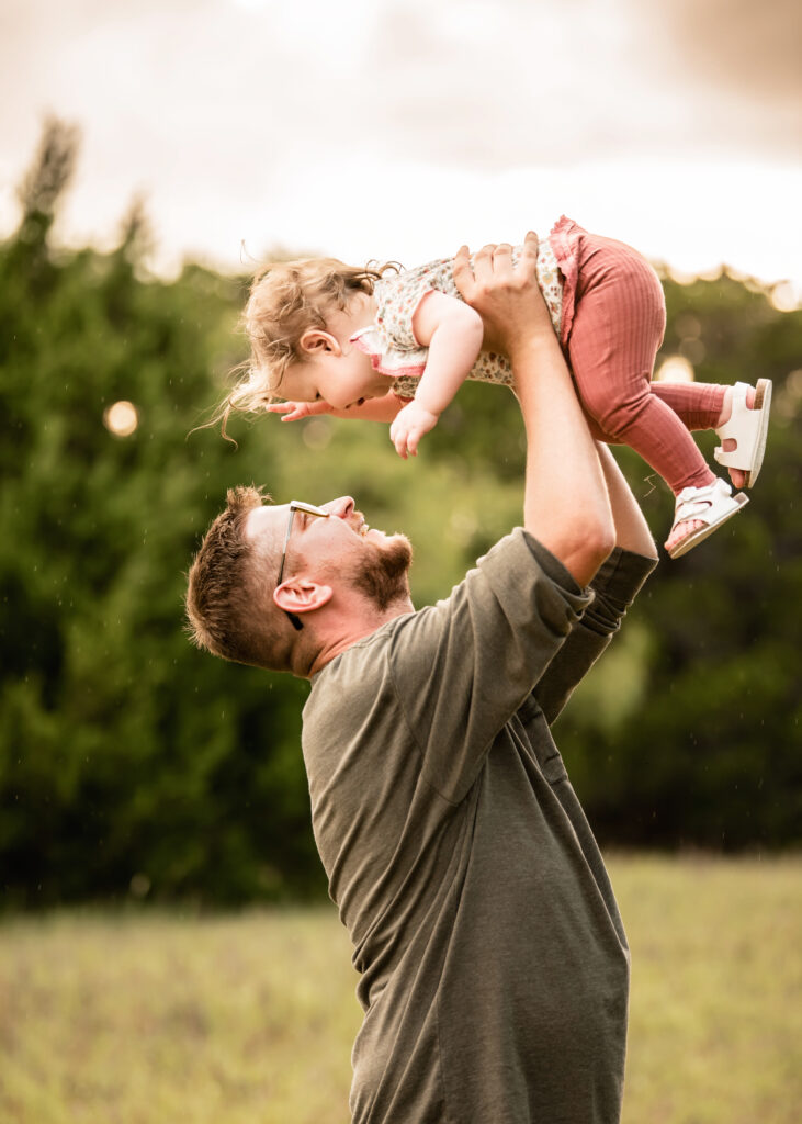 Dad lifting child in the air and laughing in a field Waco Fall Festival