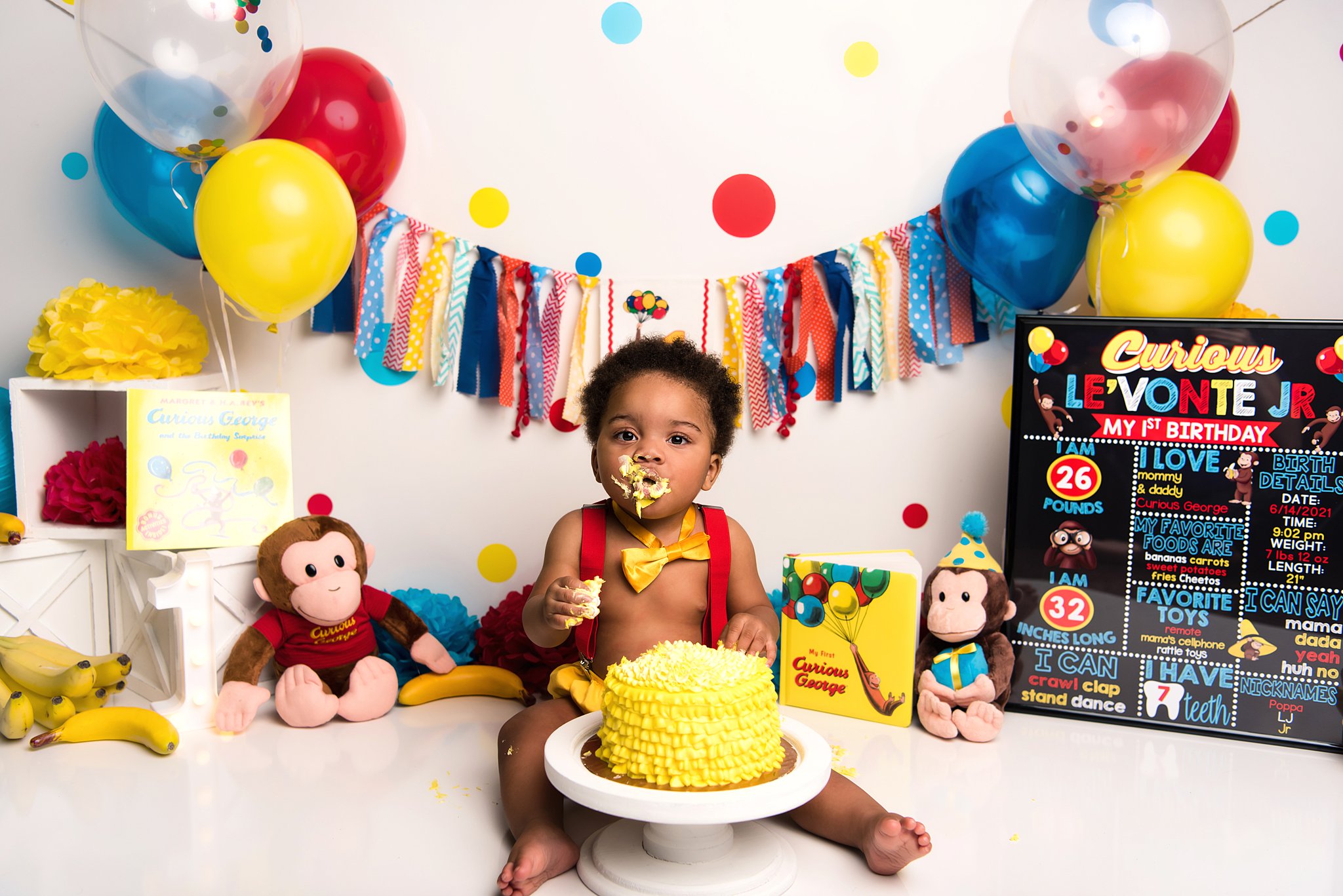 toddler boy sits in a curious george theme studio for to smash his yellow first birthday cake with some on his face luv 2 play killeen tx
