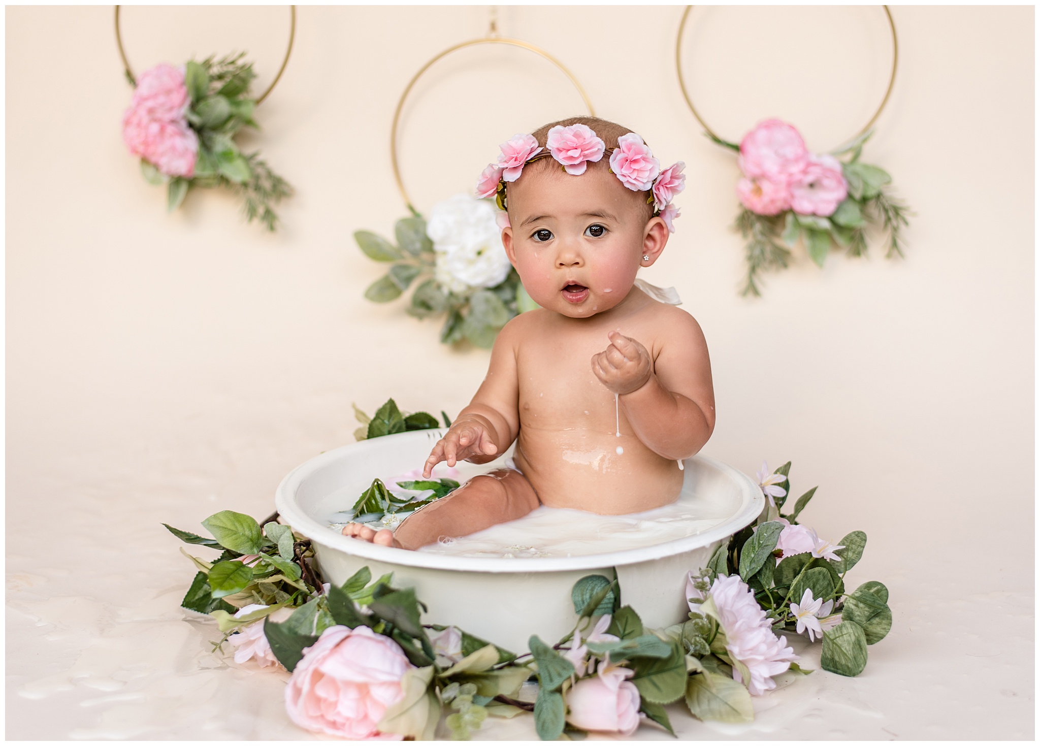 A young toddler sits naked in a wash bucket surrounded by pink carnations while wearing a pink carnation headband Because of You waco
