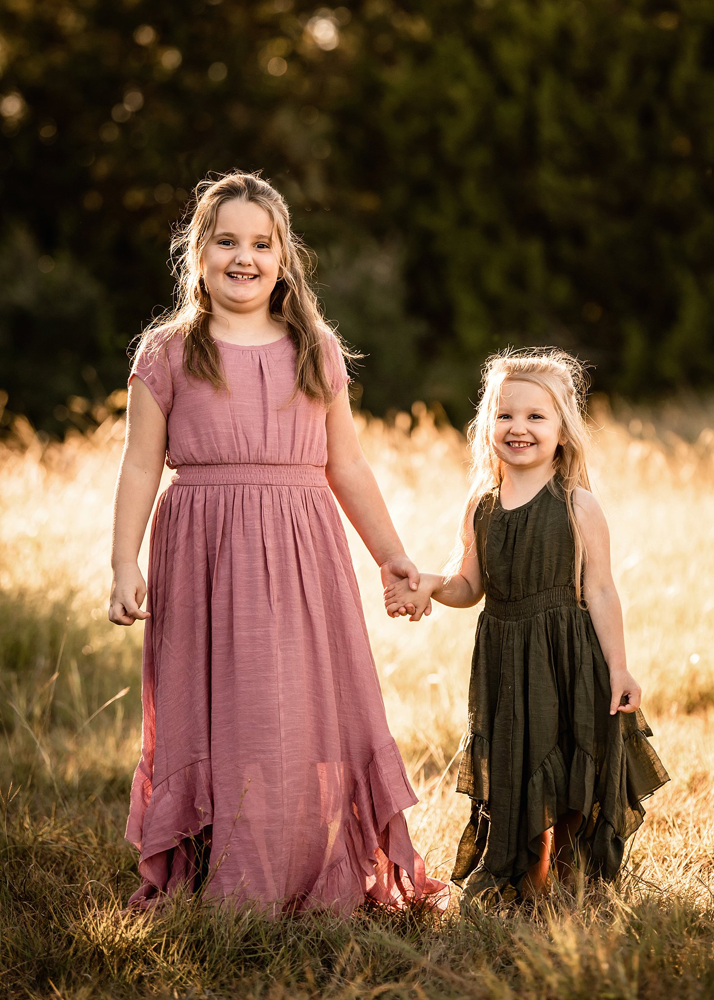 Two sisters stand in a golden grassy field holding hands in a pink and green dress waco homeschool co op