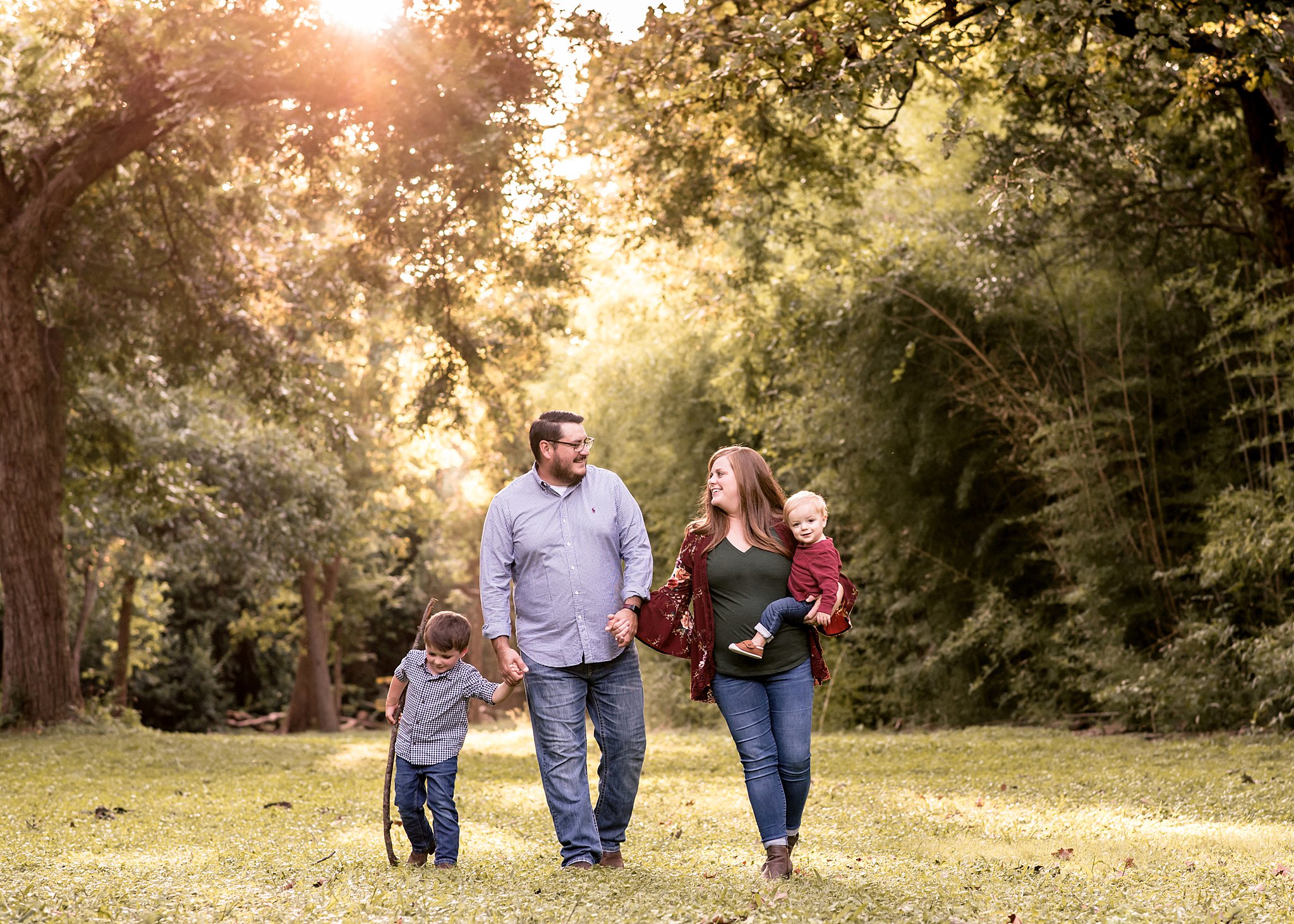 A mom with a young toddler on her hip walks through a grassy park field with her husband and older son waco homeschool co op