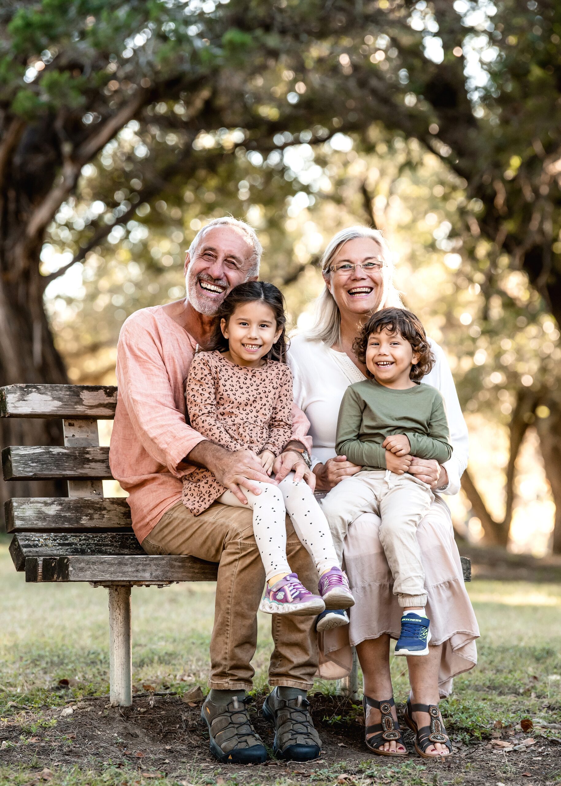 Grandma and Grandpa sit on a wooden park bench with their two grandchildren in their laps