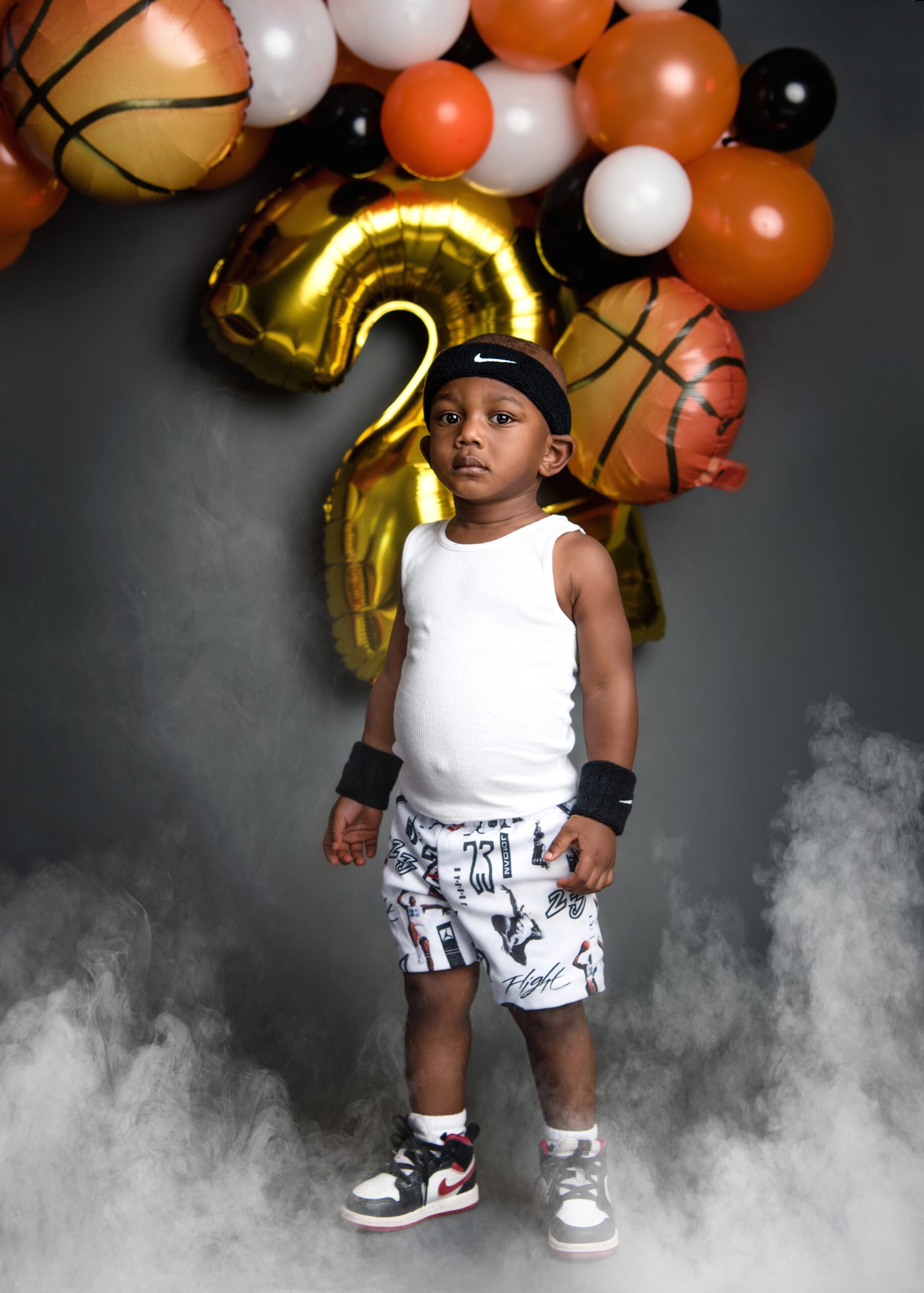A young boy in a basketball outfit stands in ground fog in a studio for his 2nd birthday party for birthday parties waco tx