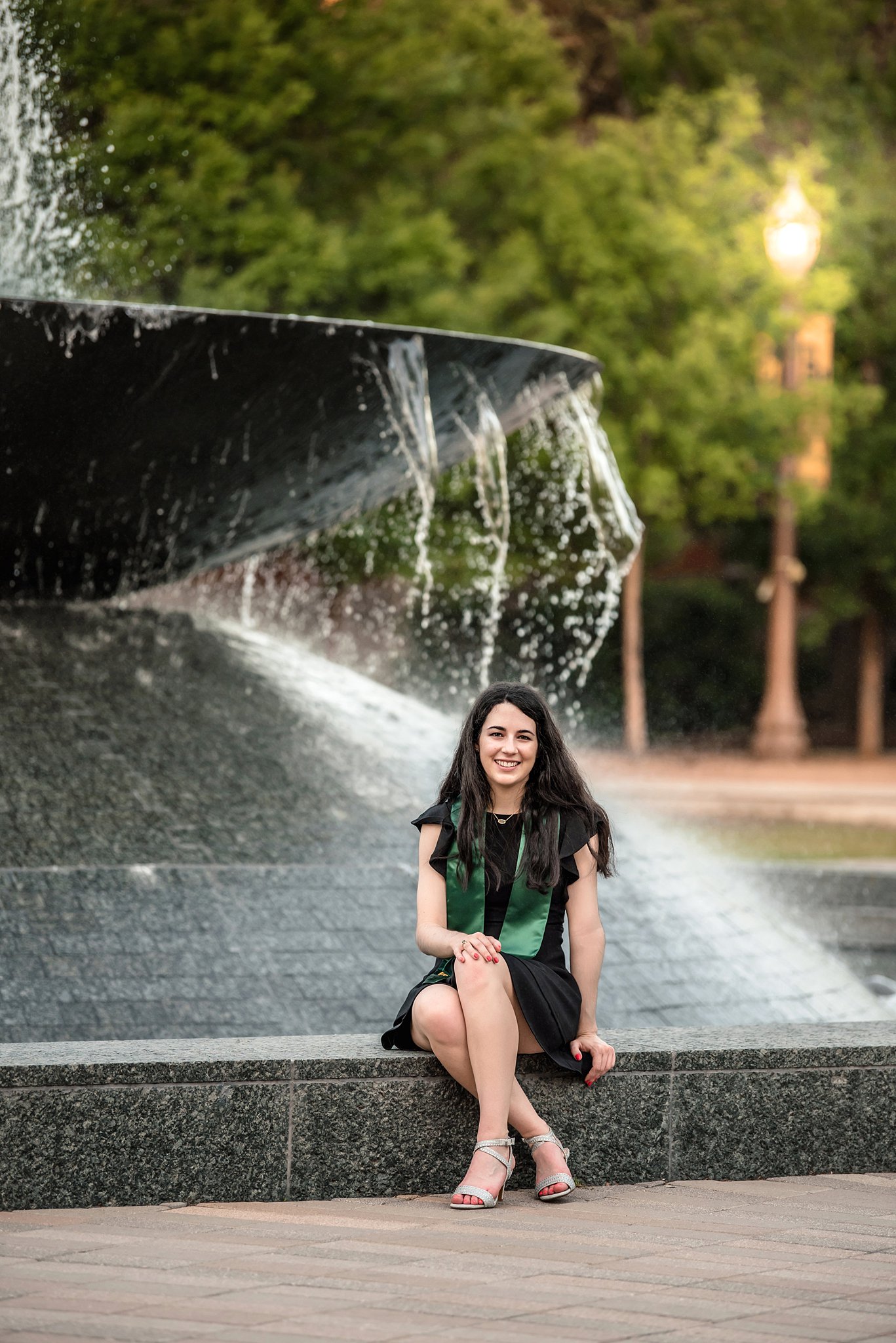 A college graduate sits on the edge of a black fountain wearing her stole at colleges waco texas