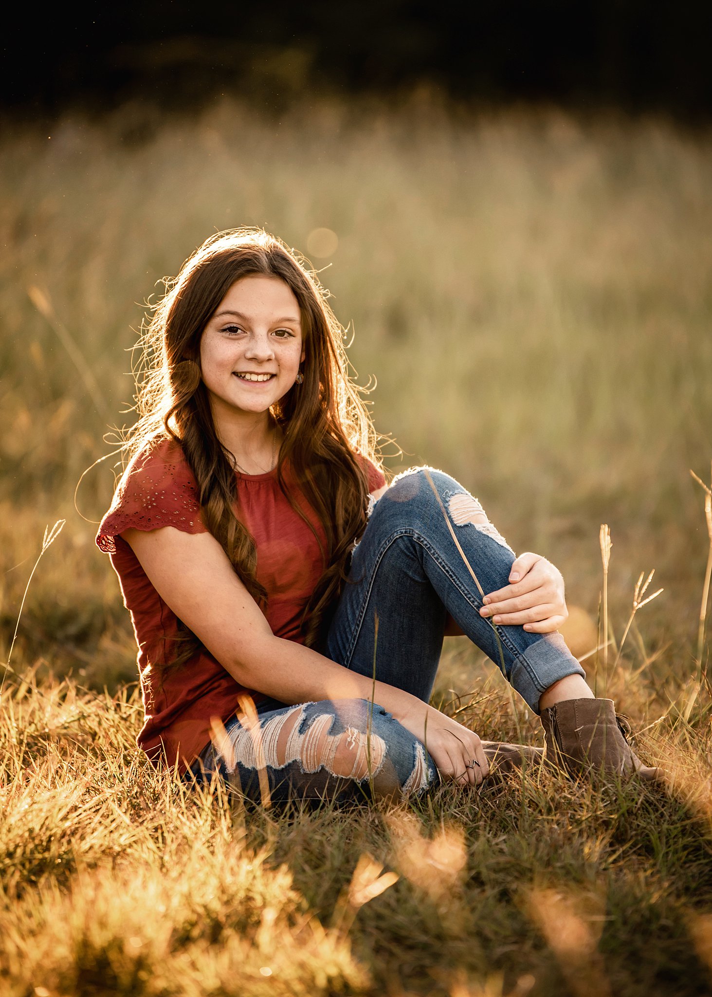 A young girl sits in a field at sunset in jeans and a red shirt after attending a waco montessori school