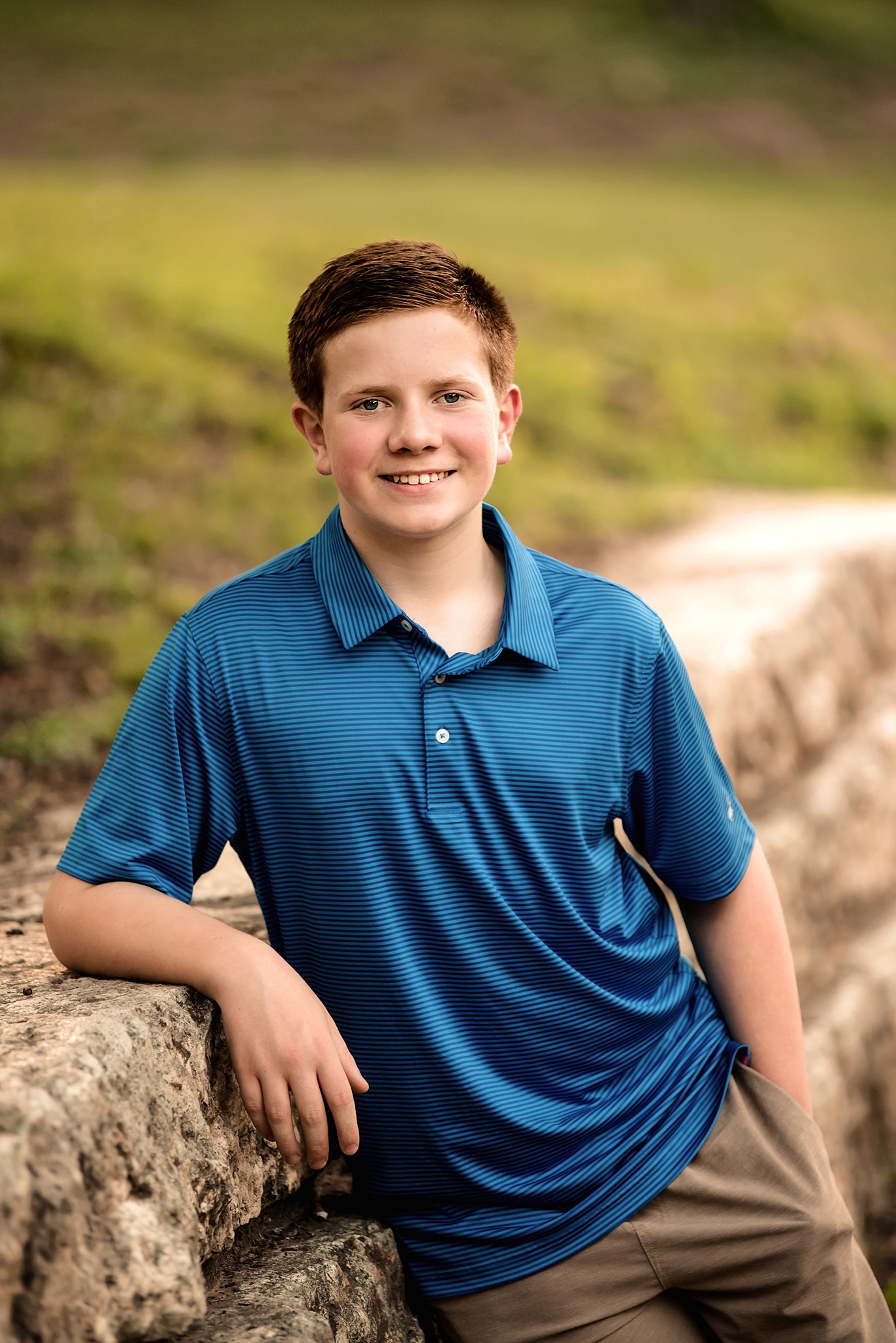 A high school senior leans against a stone wall in a blue polo shirt after attending waco montessori school