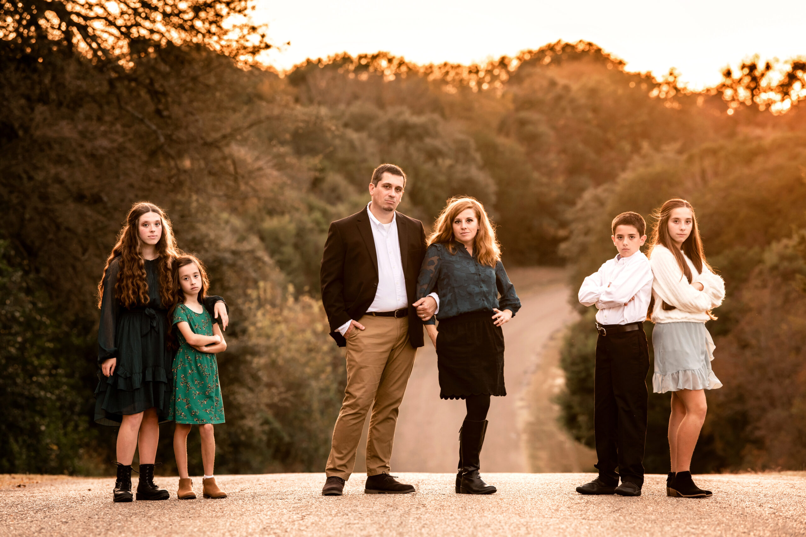 A mom and dad stand in a rural road with their four children leaning on each other on either side at sunset