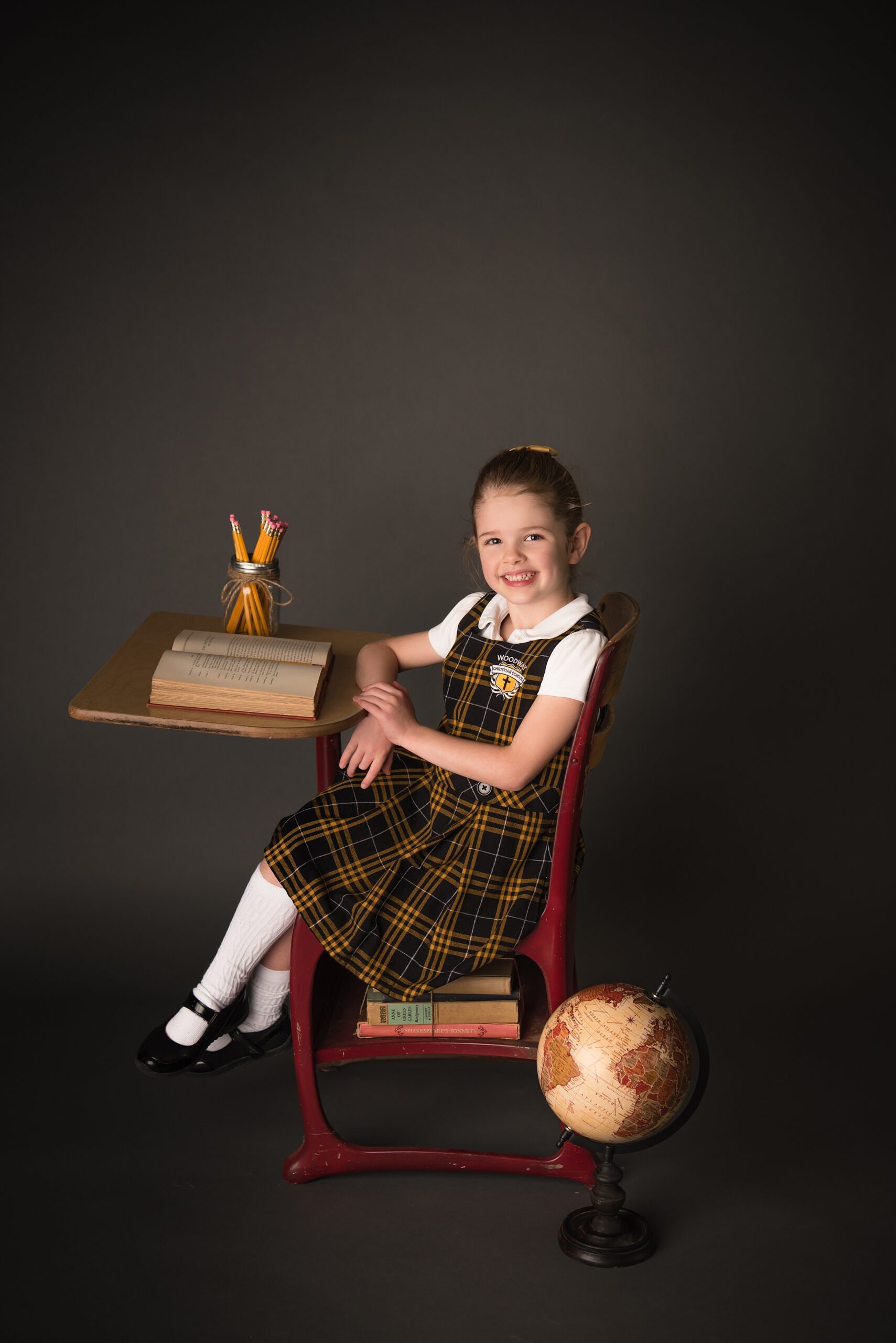 A young girl in a school uniform sits at a school desk in a studio before visiting playgrounds waco tx