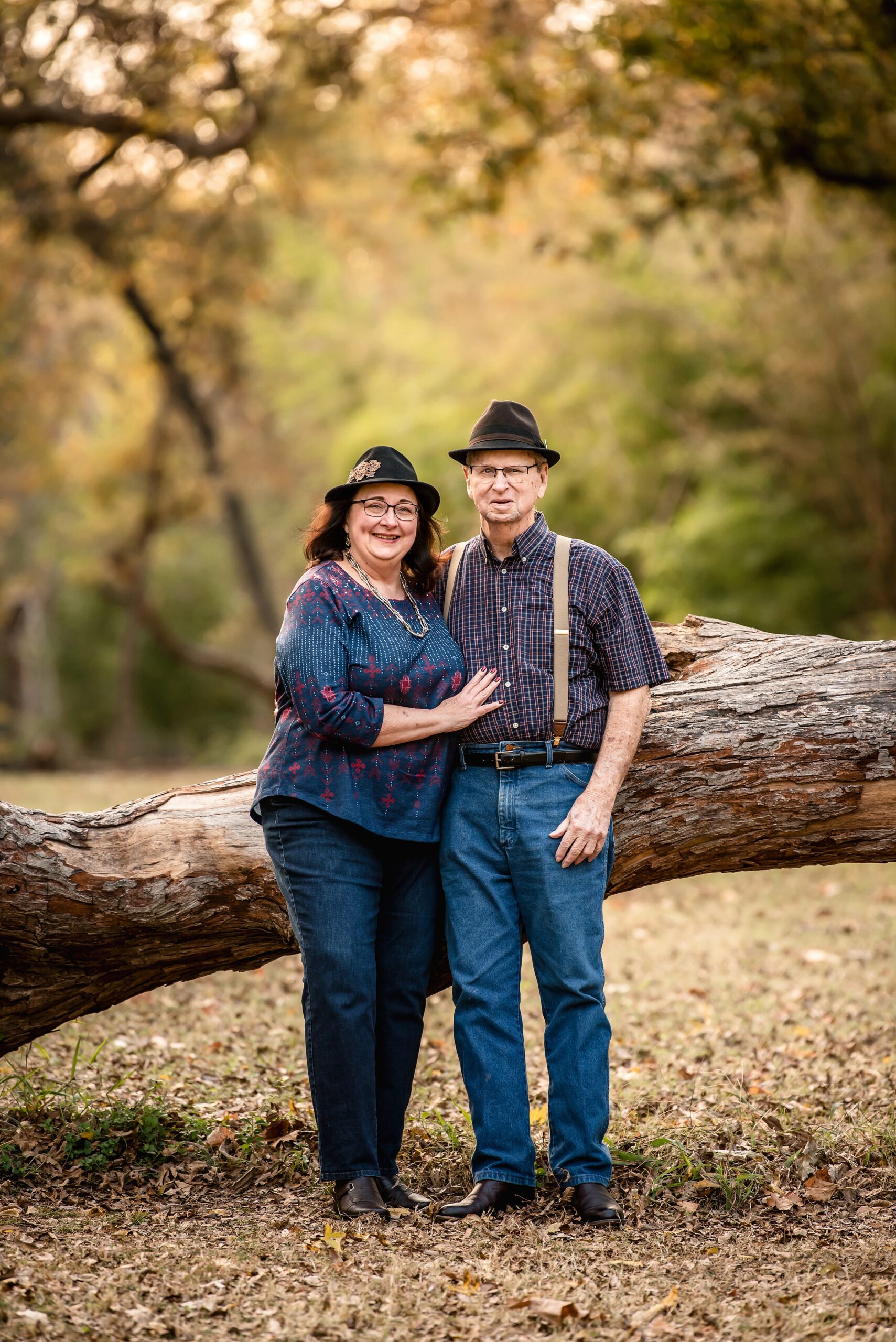 An older couple in jeans stand against a fallen tree in a park at sunset before date ideas in waco